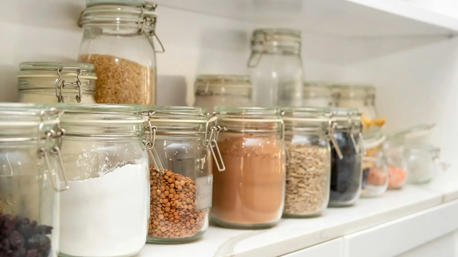 Pantry shelf lined with matching glass storage jars of dry goods
